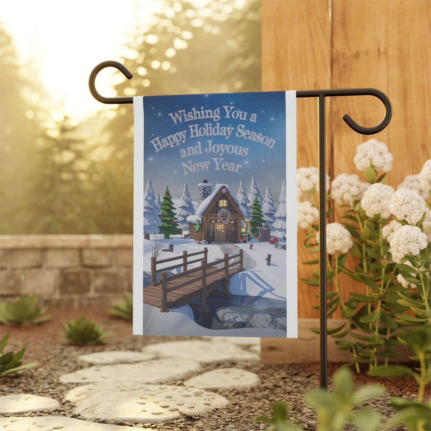 Festive garden banner with holiday greeting, featuring a snowy cabin scene, displayed on a garden flag stand among flowers.