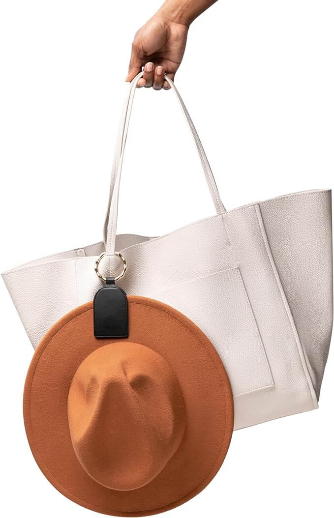 Magnetic hat holder clip on white tote bag with brown hat, showcasing hands-free travel accessory for secure hat attachment.