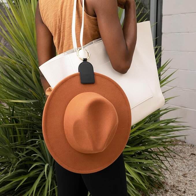 Woman carrying a tote bag with a magnetic hat holder clip attached, securing a brown hat.