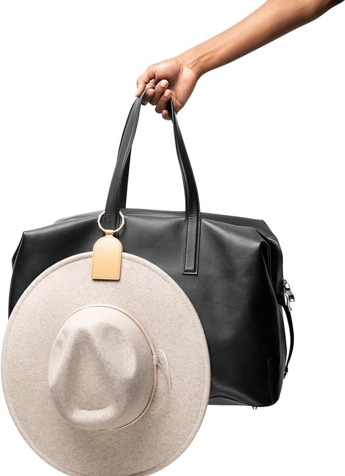 Magnetic hat holder clip for bags, shown with beige hat attached to a black travel bag, showcasing hands-free design and durability.