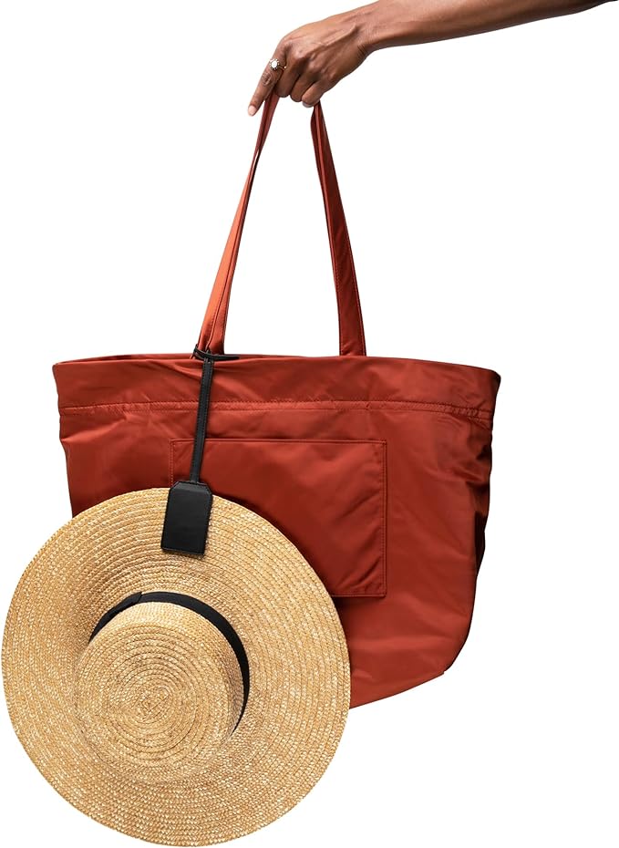 "DKMO The Loop Magnetic Hat Clip Holder securing a straw hat to a red tote bag, showcasing innovative design for travel convenience."